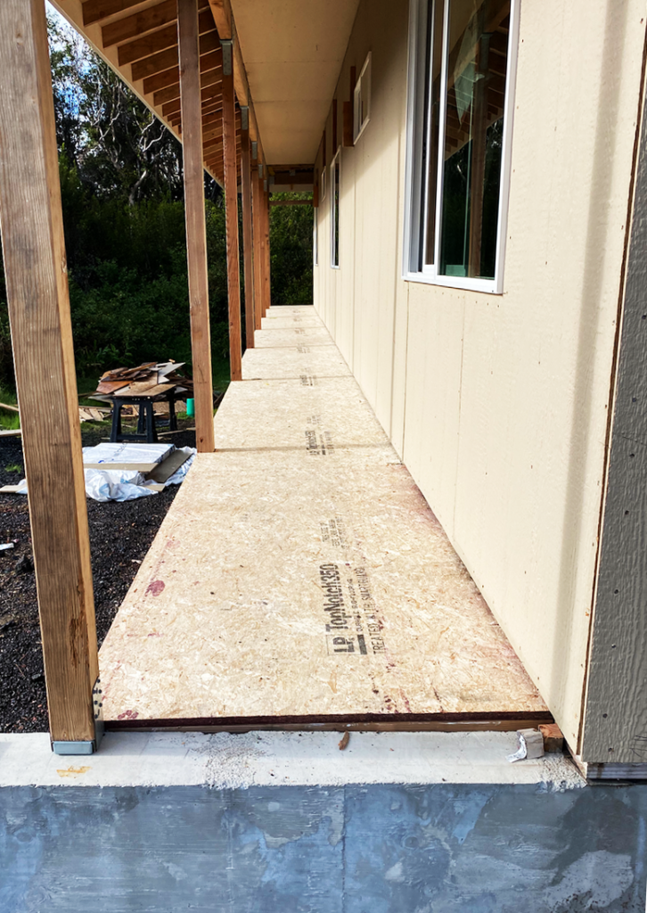 Construction of a covered porch walkway with OSB flooring and wooden posts.